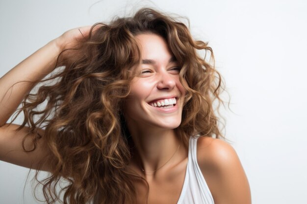 La giovane donna graziosa sorridente sta tenendo i capelli sul viso mentre sorride su sfondo bianco