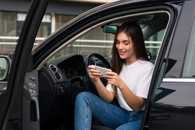 La giovane donna graziosa usa il telefono mentre era seduto nella sua nuova auto