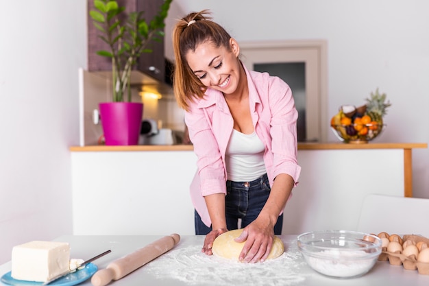 La giovane donna impasta la pasta alla cucina, fabbricazione del forno casalinga. Pasta d'impastamento della donna sul tavolo da cucina