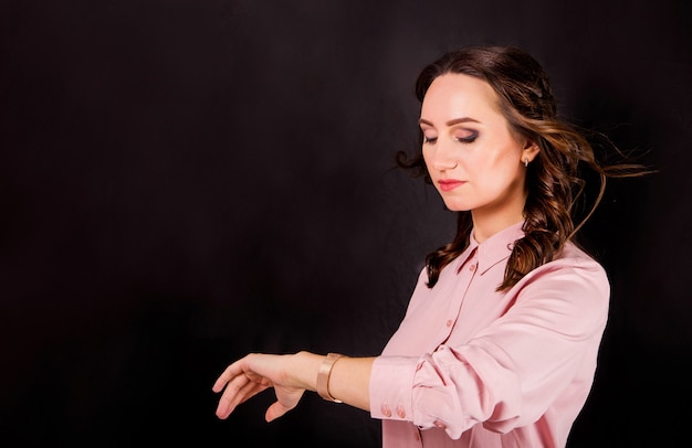 La giovane donna in blusa rosa su fondo nero esamina l'orologio