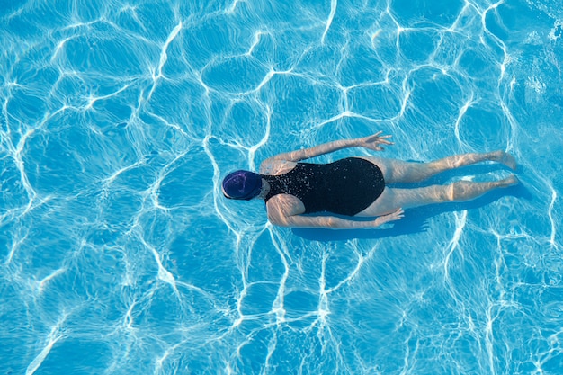 La giovane donna in cappuccio mette in mostra il costume da bagno che nuota underwater nello stagno blu