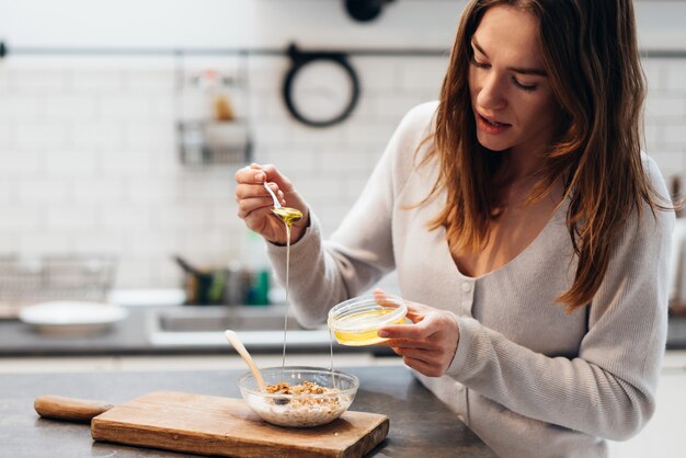 La giovane donna in cucina aggiunge miele al muesli.