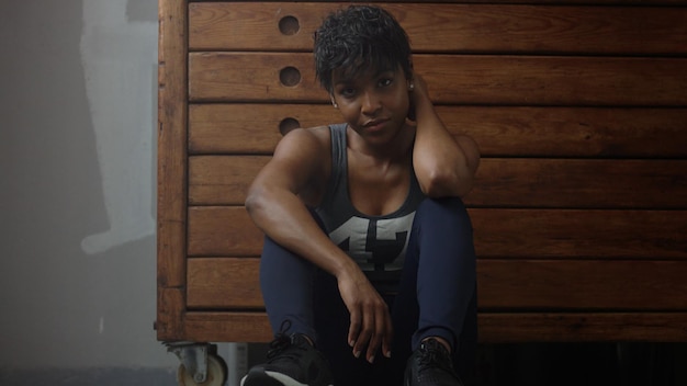La giovane donna in forma e tonificante si siede magra sull'armadio in legno durante il riposo di allenamento in loft