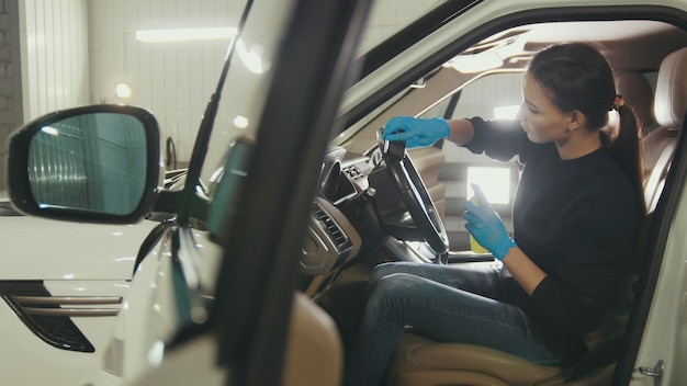 La giovane donna in guanti blu sta pulendo l'interno dell'auto per un SUV di lusso, primo piano