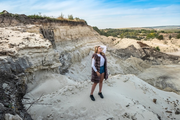 La giovane donna in pelliccia posa nelle rocce o nel canyon della sabbia. vacanza, libertà