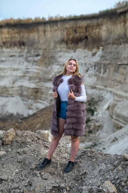 La giovane donna in pelliccia posa nelle rocce o nel canyon della sabbia. vacanza, libertà