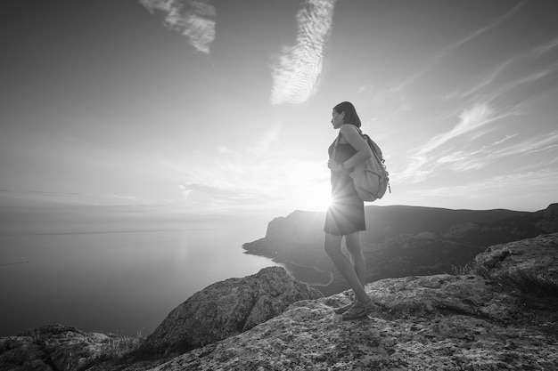 La giovane donna in un abito sportivo con zaino gode della vista delle montagne e del mare al tramonto. Concetto di viaggio e stile di vita attivo. Glamping