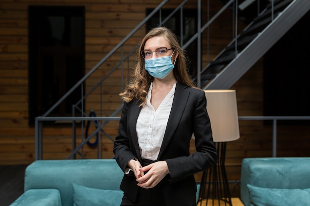 La giovane donna in un tailleur nero guarda la telecamera indossando una maschera medica protettiva sul viso
