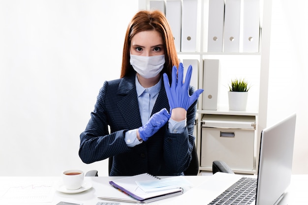 La giovane donna in una maschera protettiva indossa guanti protettivi. Donna d'affari in una maschera medica sul posto di lavoro.