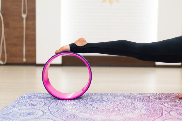 La giovane donna in uno yoga degli abiti sportivi si esercita con una ruota di yoga nella palestra