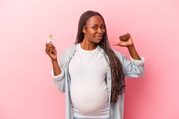 La giovane donna incinta afroamericana che tiene il ciuccio isolato su sfondo rosa si sente orgogliosa e sicura di sé, esempio da seguire.