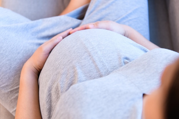 La giovane donna incinta che si siede sul sofà e tiene la sua pancia durante vedere un medico all&#39;ospedale