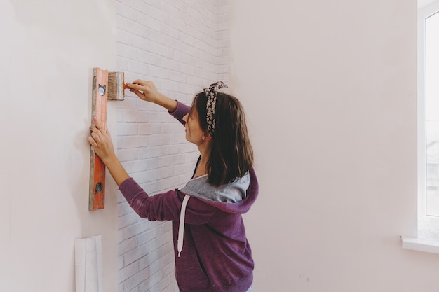 La giovane donna incolla la carta da parati a casa. la ragazza incolla la carta da parati a forma di mattone. riparazione.