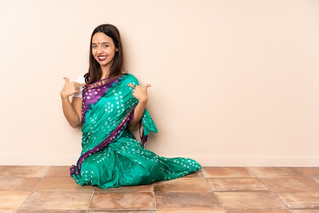 La giovane donna indiana che si siede sul pavimento che dà un pollice aumenta il gesto