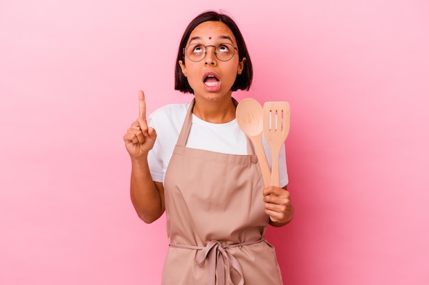 La giovane donna indiana del cuoco che tiene un cucchiaio di legno e una forchetta ha isolato il rialzo di puntamento con la bocca aperta.