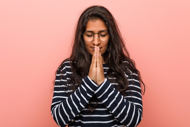 La giovane donna indiana intellettuale che si tiene per mano nella preghiera vicino alla bocca, si sente sicura.