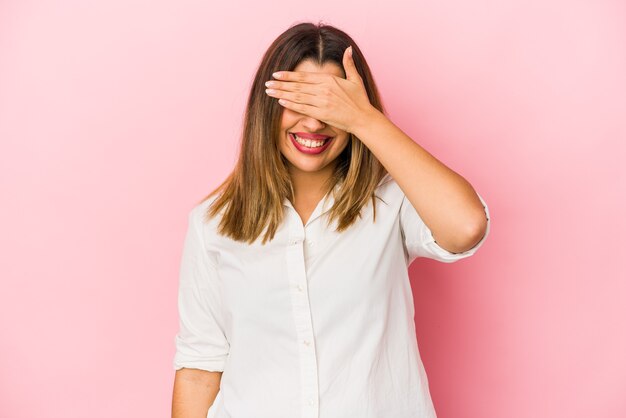 La giovane donna indiana isolata sulla parete rosa copre gli occhi con le mani, sorride ampiamente in attesa di una sorpresa.