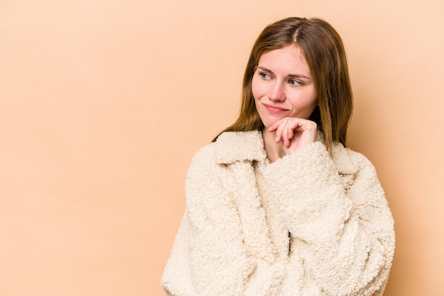 La giovane donna inglese isolata su sfondo beige si è rilassata pensando a qualcosa guardando uno spazio di copia