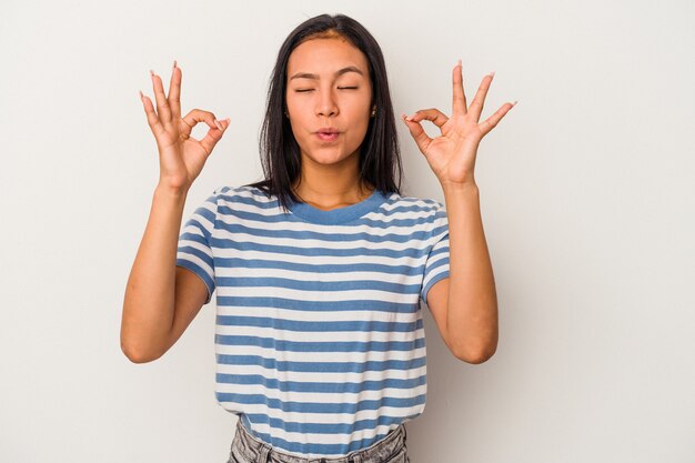 La giovane donna latina isolata su fondo bianco si rilassa dopo una dura giornata di lavoro, sta eseguendo lo yoga.