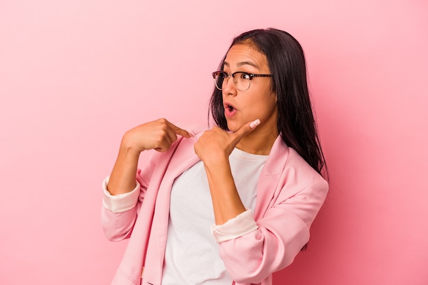 La giovane donna latina isolata su fondo rosa ha sorpreso indicando con il dito, sorridendo ampiamente.