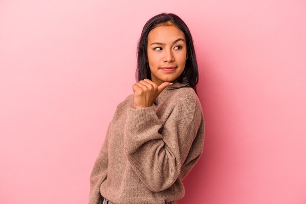 La giovane donna latina isolata su sfondo rosa punta con il pollice lontano, ridendo e spensierato.