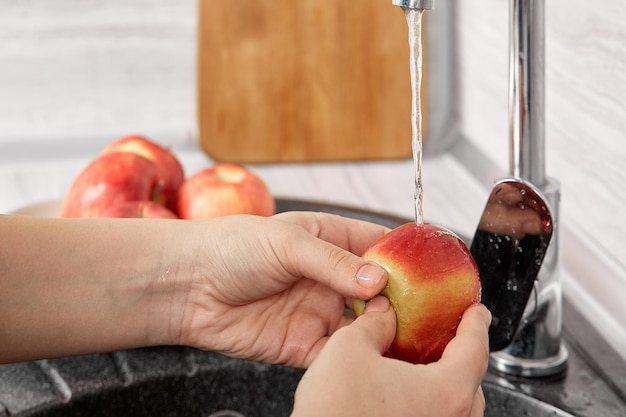 La giovane donna lava le mele mature in cucina