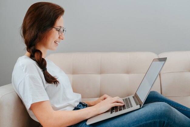 La giovane donna lavora a casa su un laptop seduto sul divano in ambiente domesticoconcetto di ordini online