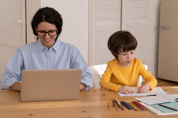 La giovane donna lavora al computer portatile mentre il figlio disegna