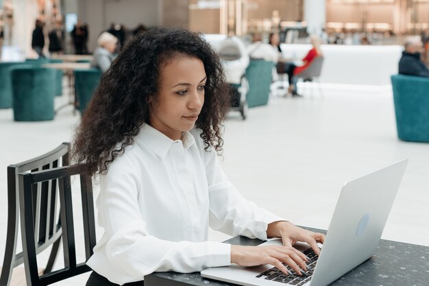 La giovane donna lavora su un computer portatile in un centro commerciale del caffè