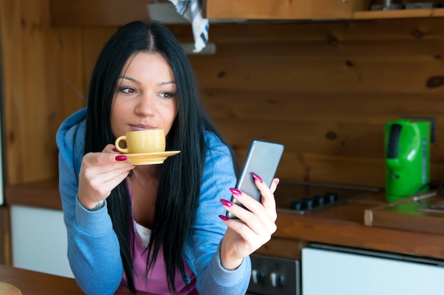 La giovane donna legge i suoi messaggi mentre beve il caffè