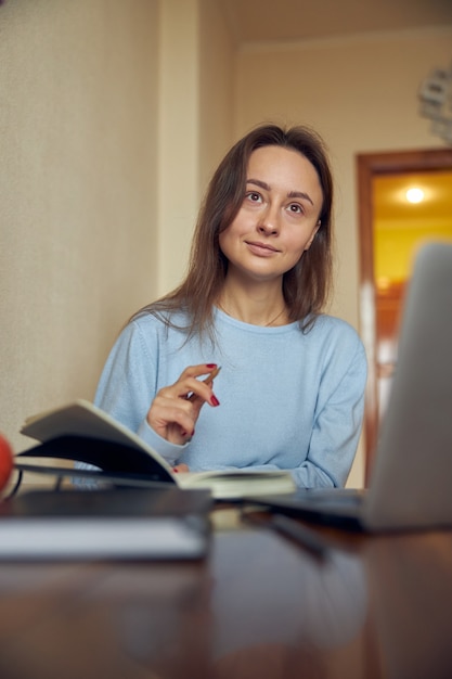 La giovane donna libera professionista allegra e sicura sta lavorando al computer portatile nella sua cucina a casa at