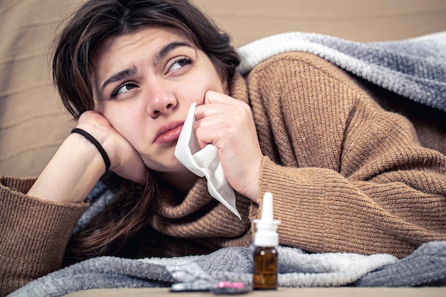 La giovane donna malata con le medicine si trova nel raffreddore del letto e nel trattamento domiciliare