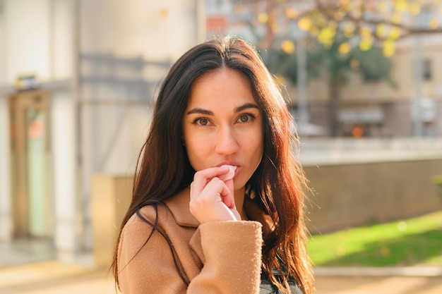 La giovane donna mangia una caramella mentre guarda la macchina fotografica per strada