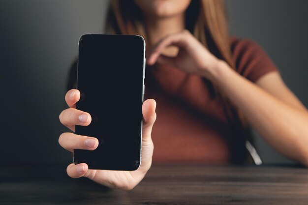 La giovane donna mostra il telefono su sfondo grigio