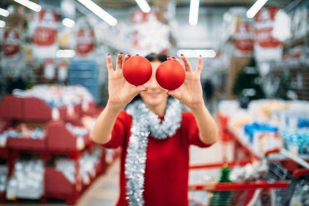 La giovane donna mostra le palle dell'albero di Natale in negozio, tradizione di famiglia. Shopping di dicembre di articoli e decorazioni natalizie