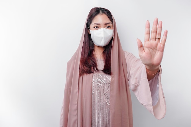 La giovane donna musulmana asiatica che indossa una maschera e l'hijab mostra il suo palmo o ferma il concetto di prevenzione covida del gesto