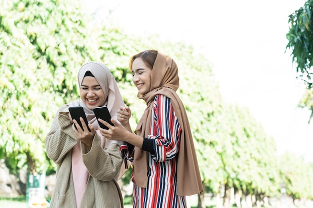 La giovane donna musulmana asiatica in foulard incontra gli amici e usa il telefono nel parco