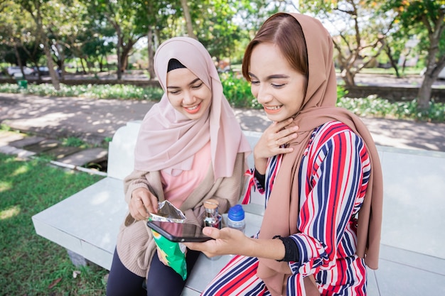 La giovane donna musulmana asiatica in sciarpa capa incontra gli amici e utilizza il telefono nel parco