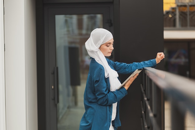 La giovane donna musulmana asiatica in sciarpa capa sorride con la compressa mobile e lo spazio della copia