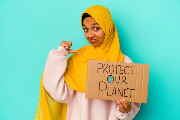 La giovane donna musulmana che tiene un protegge il nostro pianeta isolato sulla parete blu si sente orgogliosa e sicura di sé, esempio da seguire.