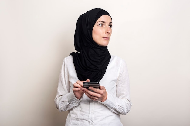 La giovane donna musulmana in hijab tiene un telefono nelle sue mani e guarda al lato