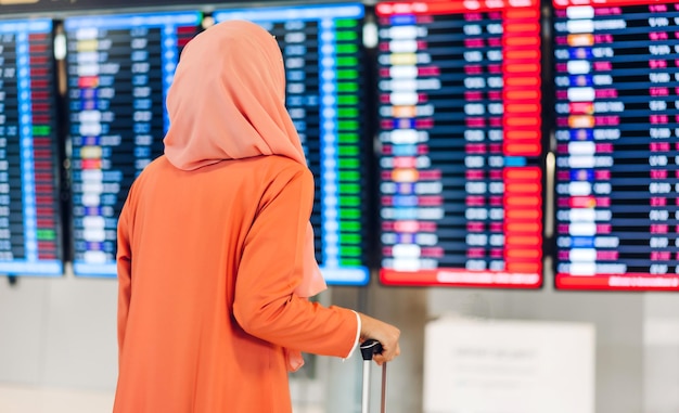 La giovane donna musulmana viaggia con i bagagli guarda il volo prima di un lungo viaggio di vacanza all'aeroporto del terminal internazionale