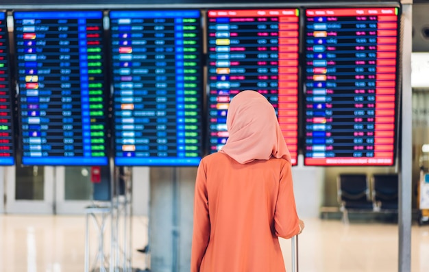 La giovane donna musulmana viaggia con i bagagli guarda il volo prima di un lungo viaggio di vacanza all'aeroporto del terminal internazionale