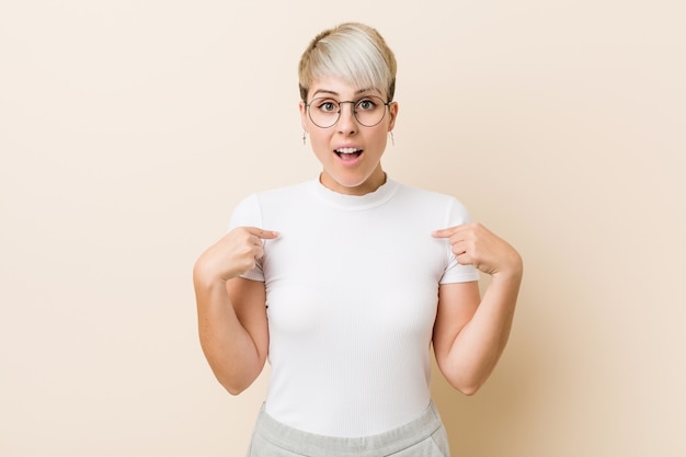 La giovane donna naturale autentica che indossa una camicia bianca ha sorpreso indicare con il dito, sorridendo ampiamente.