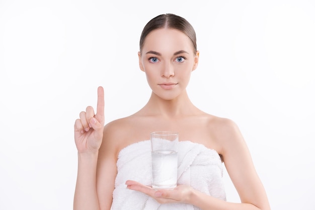 La giovane donna naturale in tovagliolo bianco tiene il bilancio idrico di concetto di bicchiere d'acqua