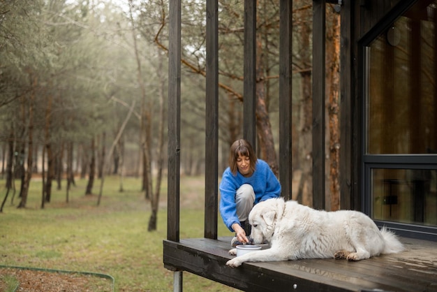 La giovane donna nutre il suo simpatico cane bianco sul portico di una casa