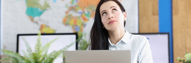 La giovane donna pensierosa si siede al computer portatile e guarda in su