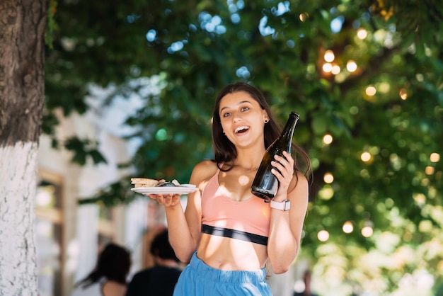 La giovane donna porta un piatto di snack e un drink in mano