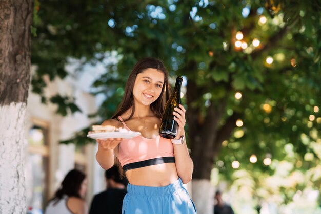 La giovane donna porta un piatto di snack e un drink in mano