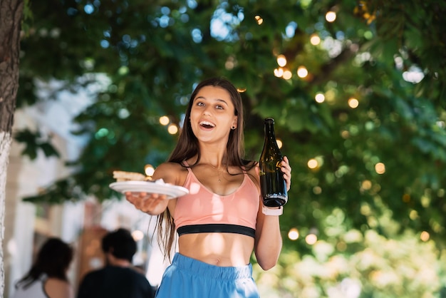 La giovane donna porta un piatto di snack e un drink in mano